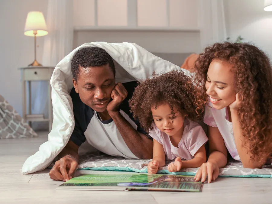 A family together at home, reading under a blanket