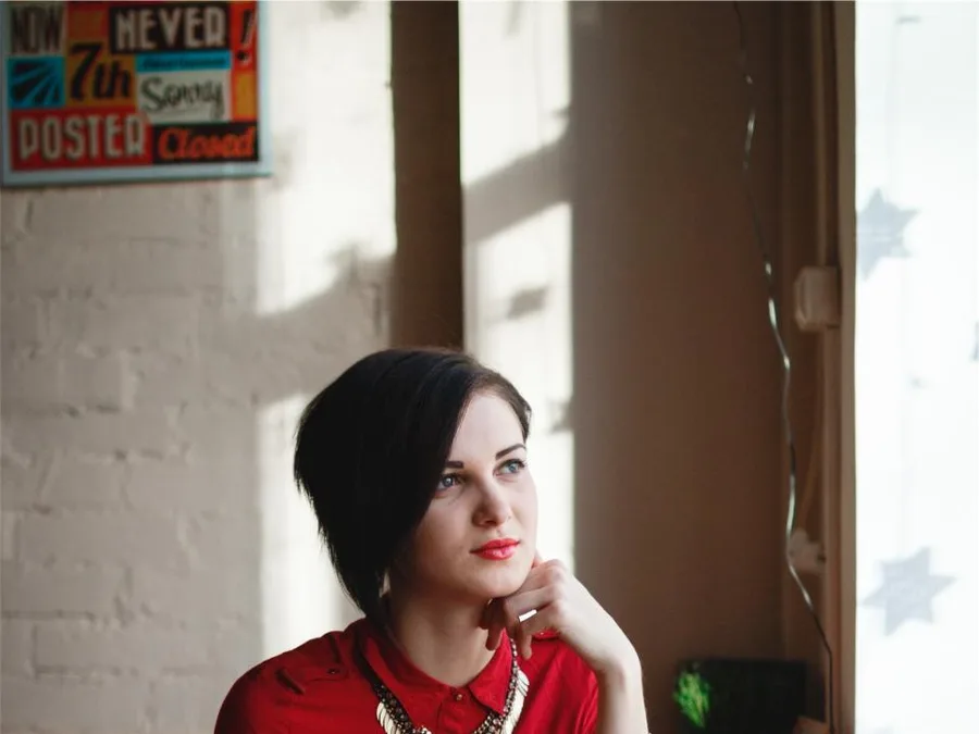 A woman sitting by a window, chin resting on her hand, looking out