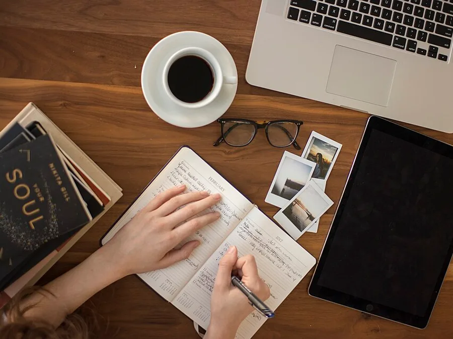 An open journal, pen and coffee on a wooden desk